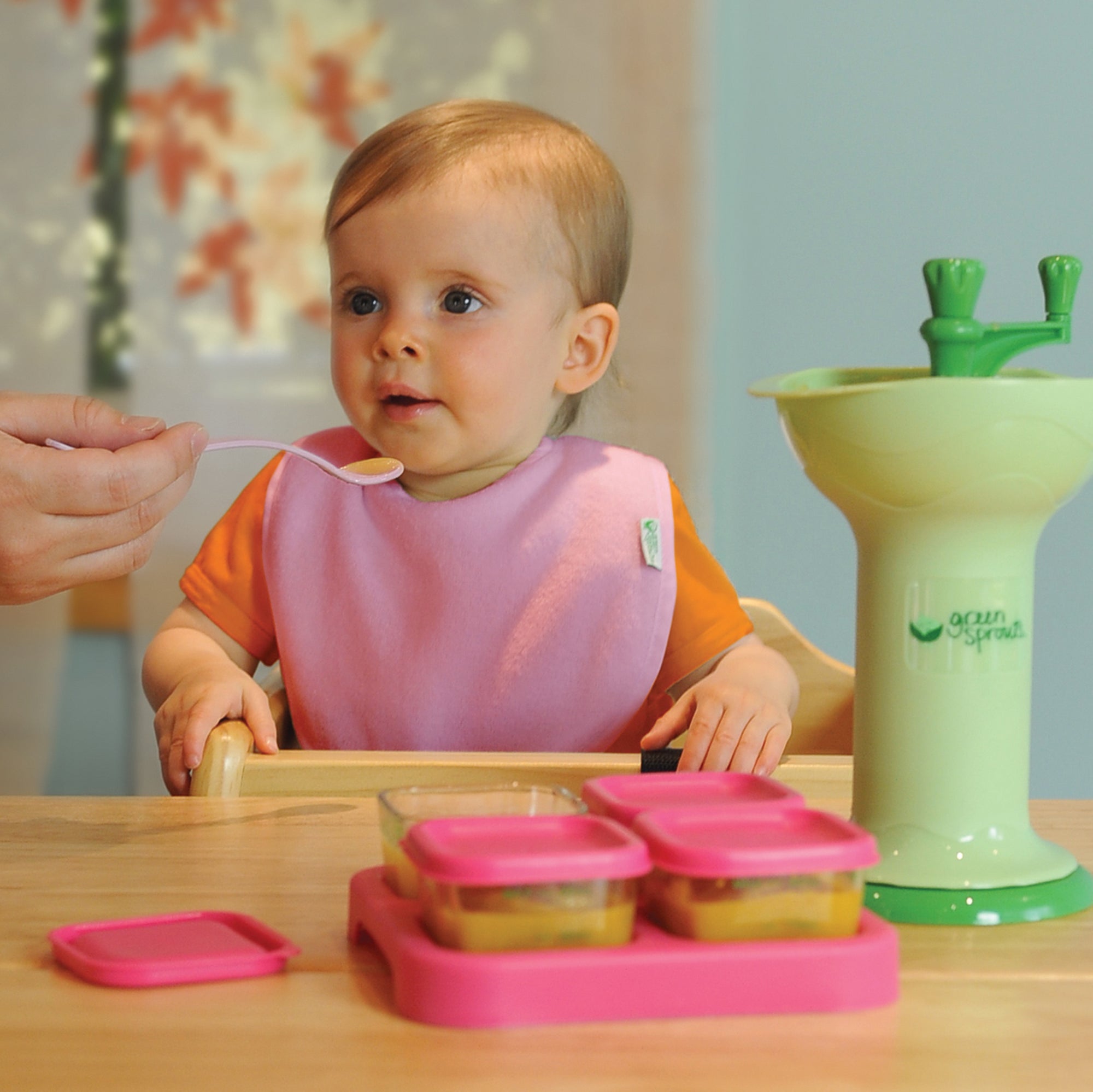 A cute baby girl enjoying the food that was used by the Fresh Baby Food Mill that is presented next to her.