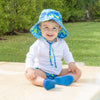 A lovable young boy sitting in the backyard smiling at the viewer while wearing Royal Blue Turtle Journey Bucket Sun Protection Hat.
