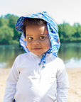 A young boy looking intently at the viewer with a little smile and his Royal Blue Sea Friends Flap Sun Protection Hat on.