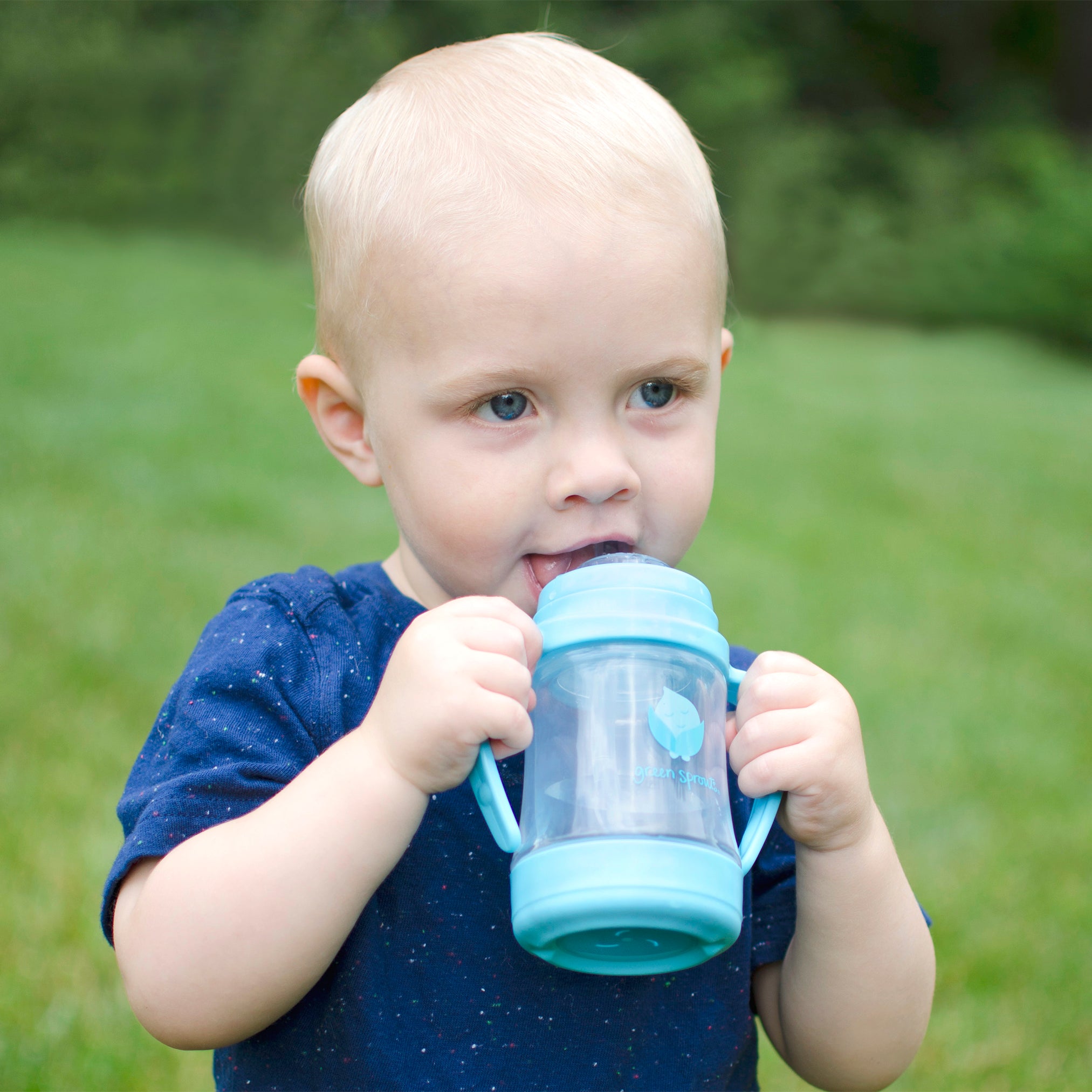 A toddler boy with a blue shirt holding a blue cup that the Glass Insert for Sip and Straw Cup.