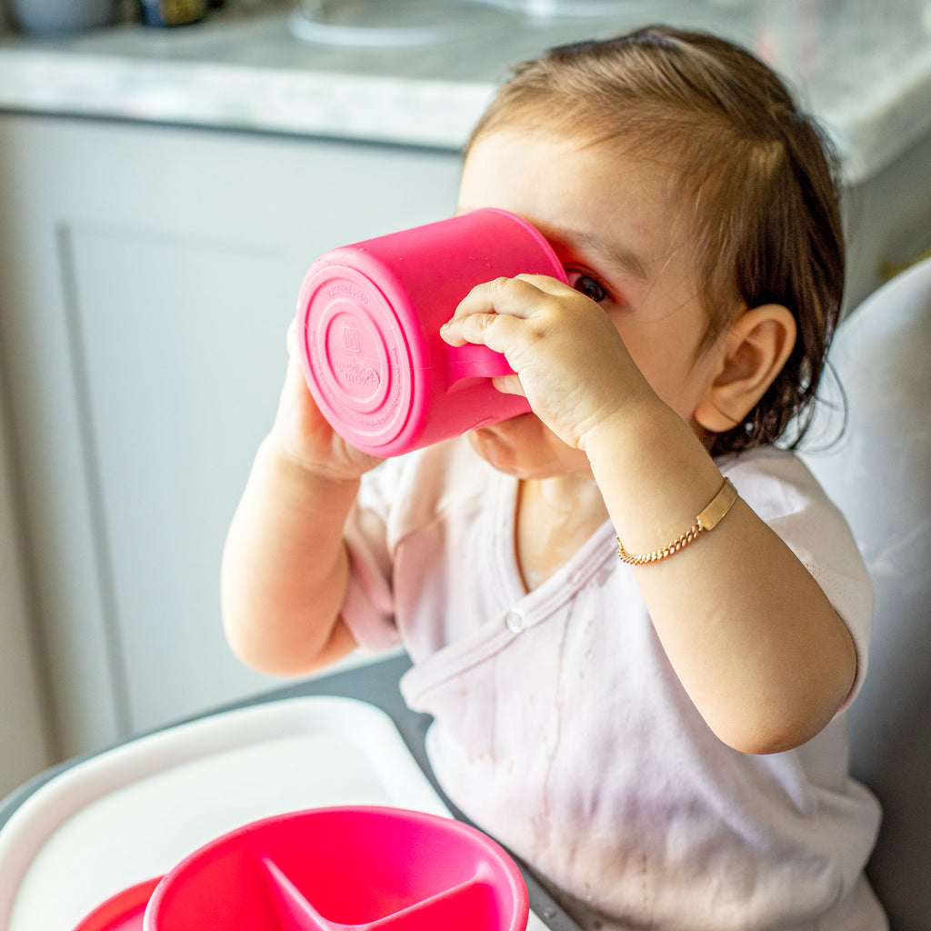 A cute little girl looking up and drinking out of her pink Learning Cup made from Silicone