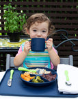 A young curly hair girl holding the navy Learning Cup made from Silicone over her mouth