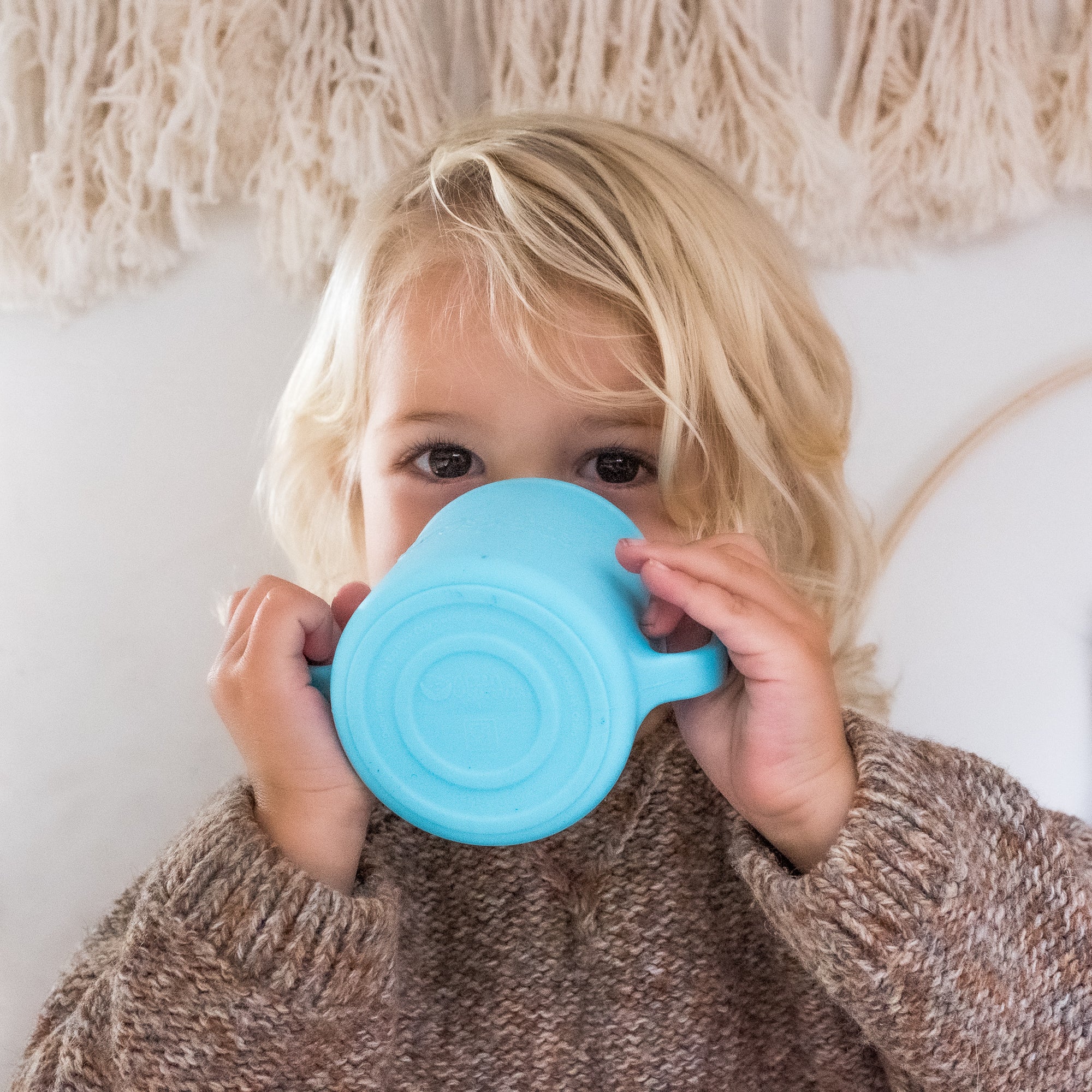A young blonde boy drinking out of the Aqua Learning Cup made from Silicone