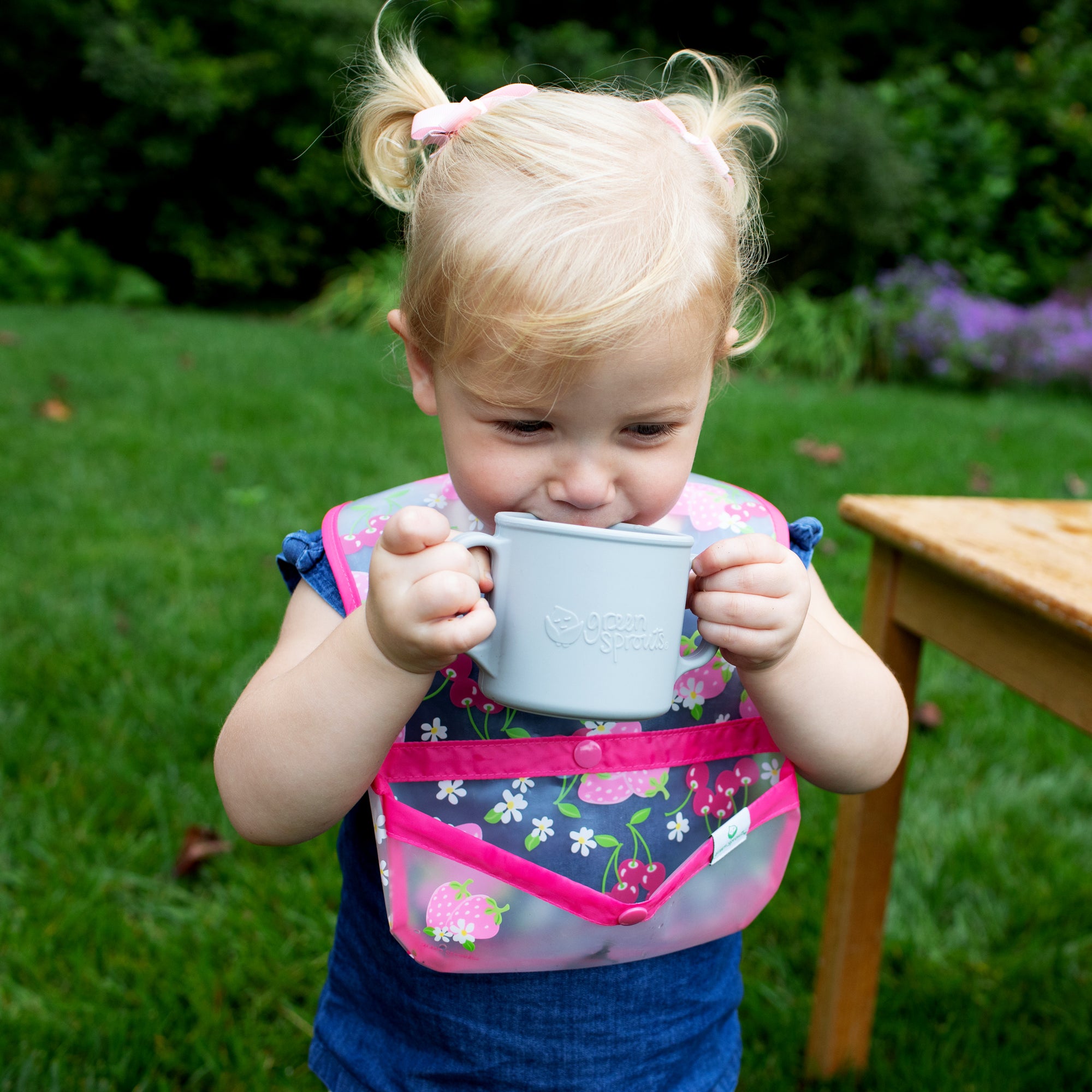 A cute little girl with pigtails trying to drink out of the gray Learning Cup made from Silicone and giggling at the same time.
