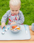 A young blond boy sitting outside looking at the food in the gray Learning Bowl made from Silicone