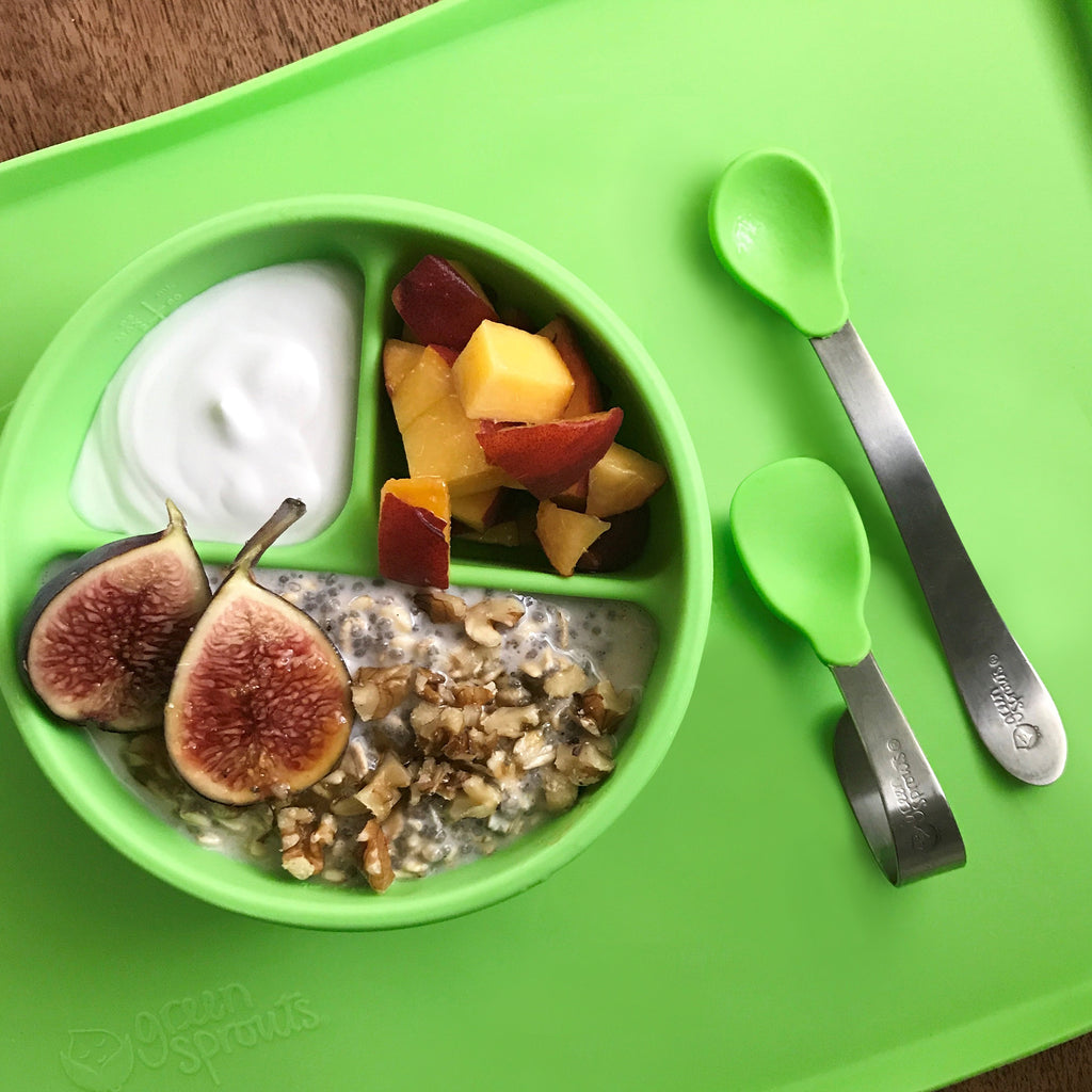 A Green Learning Spoon Set with yummy food inside the bowl sitting on green platemat.