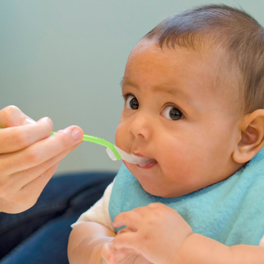 A cute little infant looking up curiously while being fed with a Green Feeding Spoon.