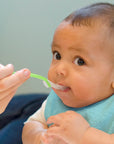 A cute little infant looking up curiously while being fed with a Green Feeding Spoon.