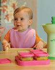 A cute baby girl enjoying the food that was used by the Fresh Baby Food Mill that is presented next to her.