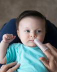 A mother with First Toothbrush made from Silicone on her finger is gently trying to coax her baby to open his mouth as he looks up at the viewer.