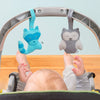 The blue raccoon and gray owl friends are attached to the handle of a carrier as a baby reaches up to play.