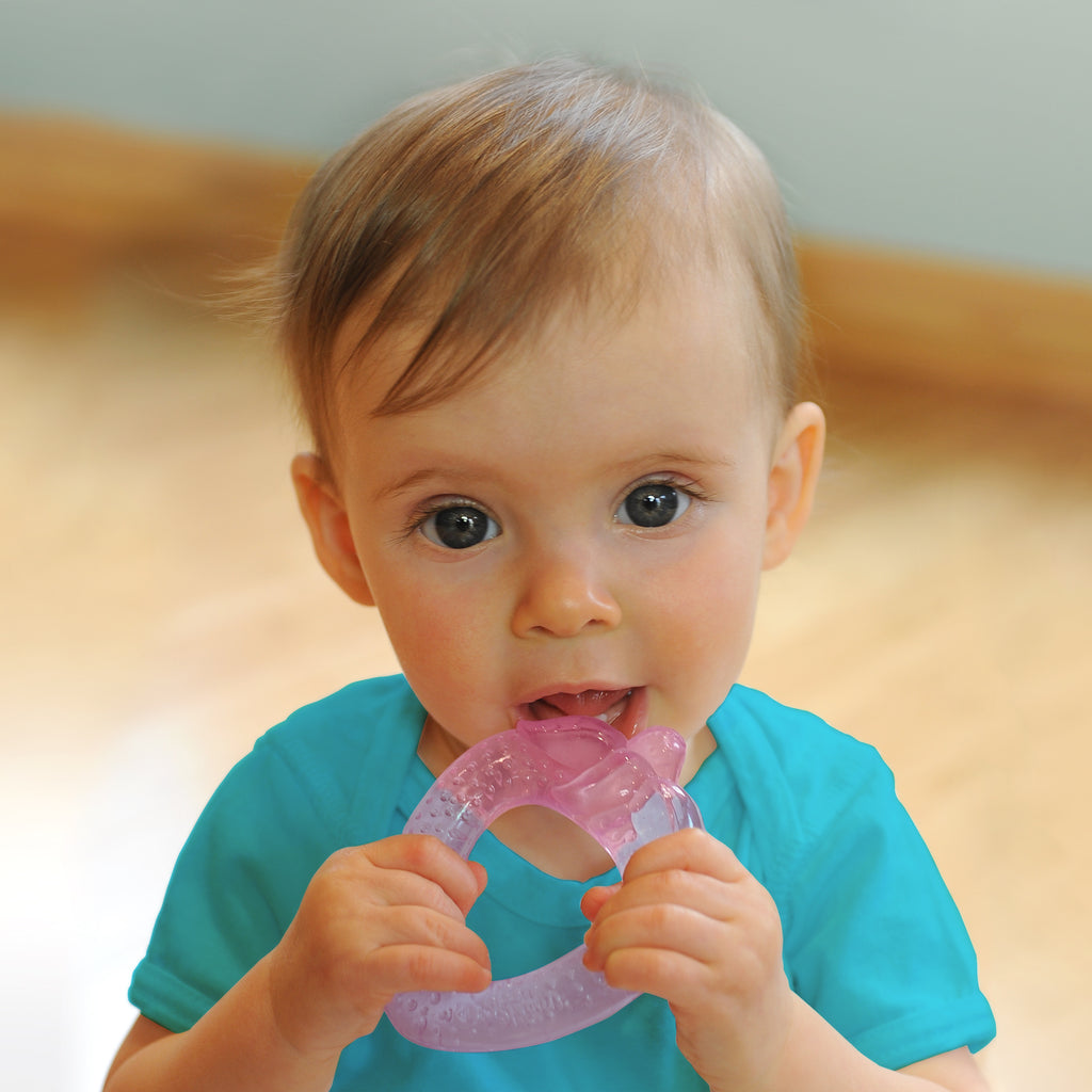 A wide-eyed 6 month old girl looking intently while gripping the light pink strawberry Cool Fruit Teether to her little mouth.