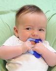 A little newborn boy laying on a green blanket and playing with the blue Everyday Teether made from Silicone in his mouth.