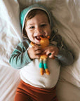 Toddler lying on a bed smiling while clutching the fox friend rattle.