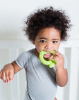 A cute little boy in a  white crib holding the green apple Fruit Teether made from Silicone in his mouth.
