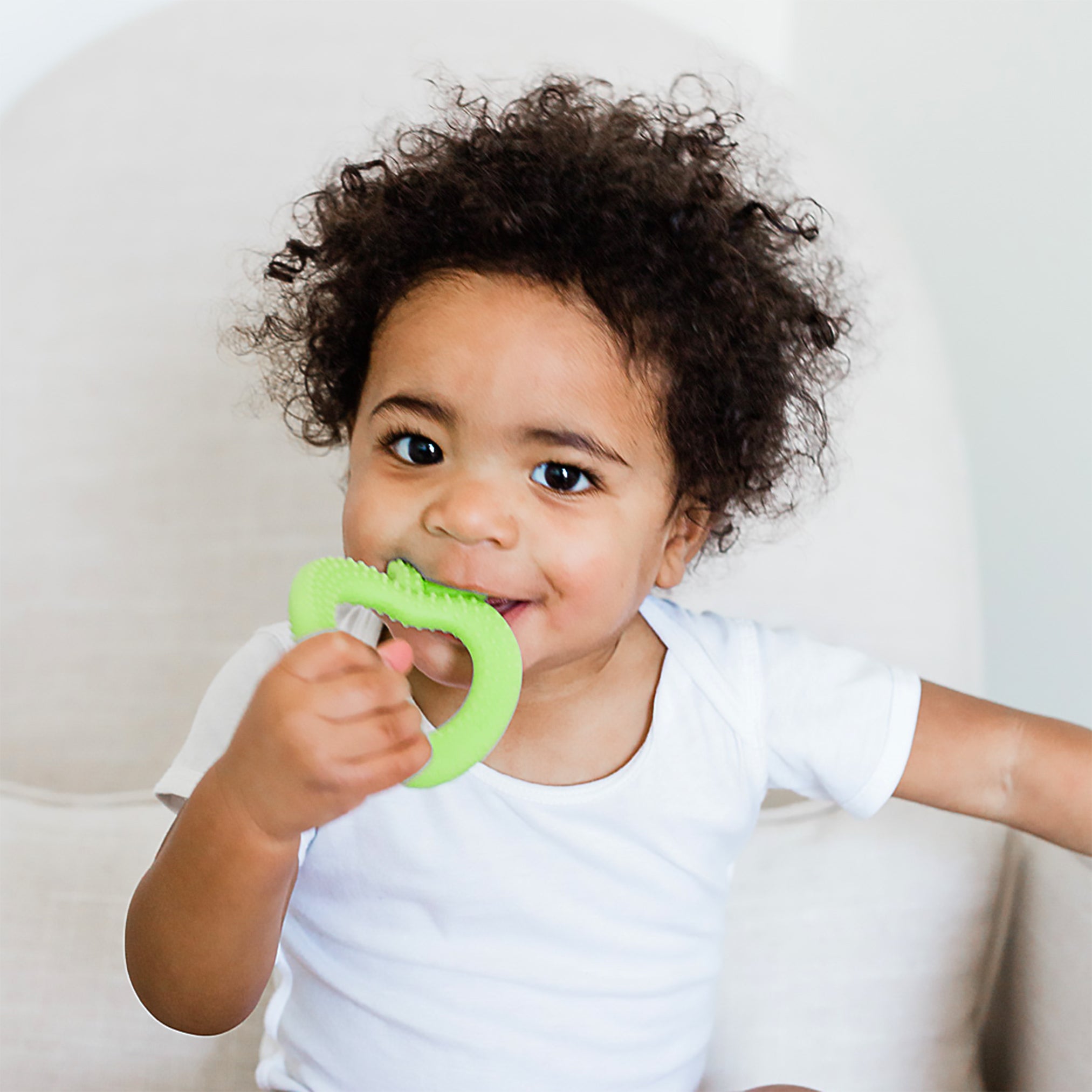 A cute little boy in a white crib holding the green apple Fruit Teether made from Silicone in his mouth.