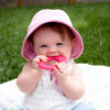 A toddler girl with a pink hat on with the Pink Strawberry Fruit Teether made from Silicone in her mouth