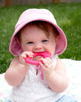 A toddler girl with a pink hat on with the Pink Strawberry Fruit Teether made from Silicone in her mouth