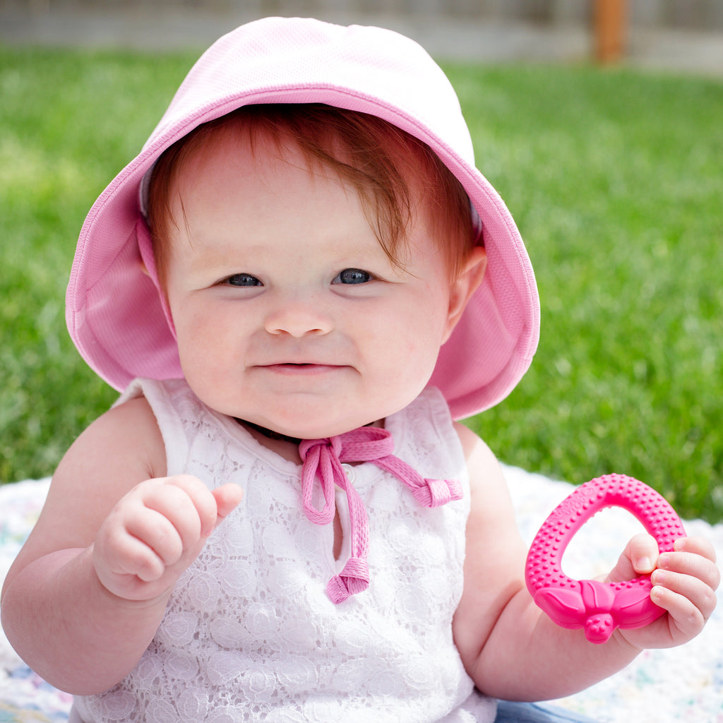 A toddler girl with a pink hat on with the Pink Strawberry Fruit Teether made from Silicone in her hand