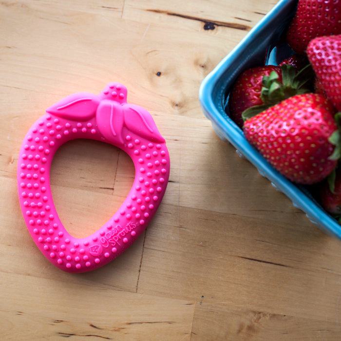 Pink Strawberry Fruit Teether made from Silicone on a table with a box full of strawberries.