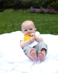 A little baby laying on a white blanket with the yellow banana Fruit Teether made from Silicone in his mouth