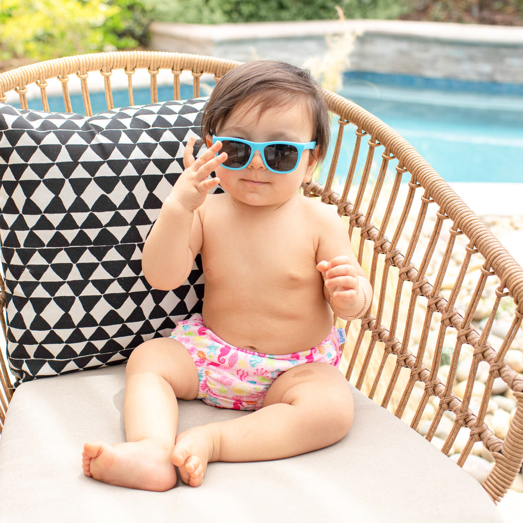 A young girl infant looking so fly in her Aqua Flexible Sunglasses while sitting in her wicker chair by the pool.