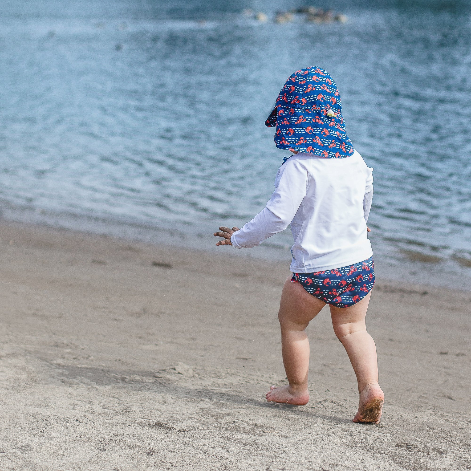 Young boy running across the sand with a white Long Sleeve Rashguard Shirt