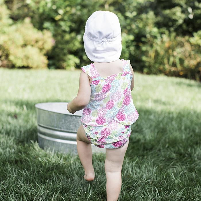 A little girl skipping through the backyard while wearing a white Breathable Swim and Sun Flap Hat.