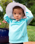 A toddler looking at the camera with her hands over her head while wearing the aqua Breathable Sun Protection Shirt.