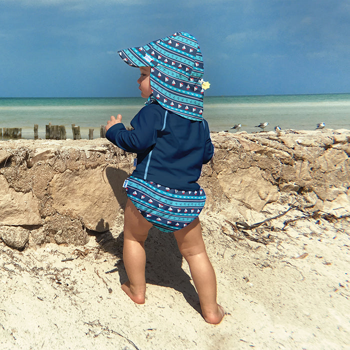 young baby standing on the beach looking a the waves while wearing a Navy Long Sleeve Rashguard Shirt