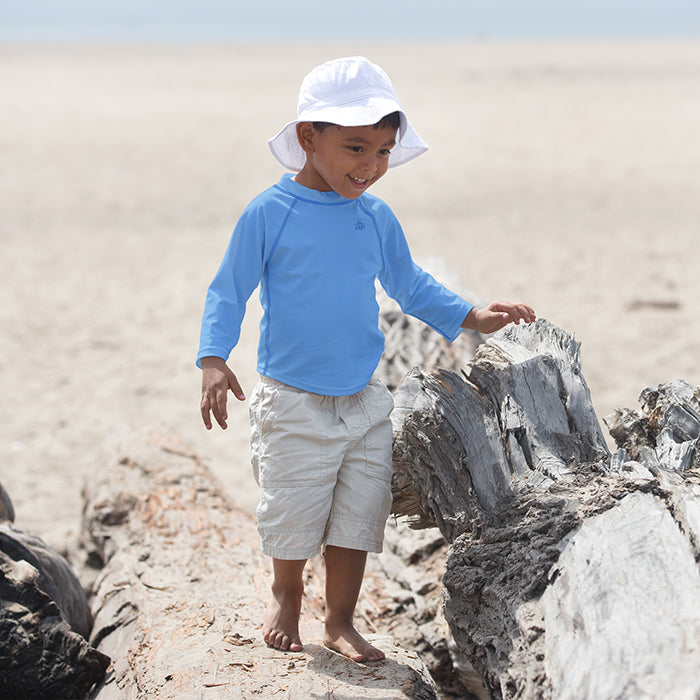 Young boy with a Light Blue Long Sleeve Rashguard Shirt inspecting the rocks on the beach