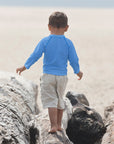 Young boy with a Light Blue Long Sleeve Rashguard Shirt walking away through the rocks on the beach