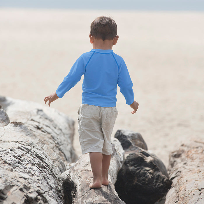 Young boy with a Light Blue Long Sleeve Rashguard Shirt walking away through the rocks on the beach